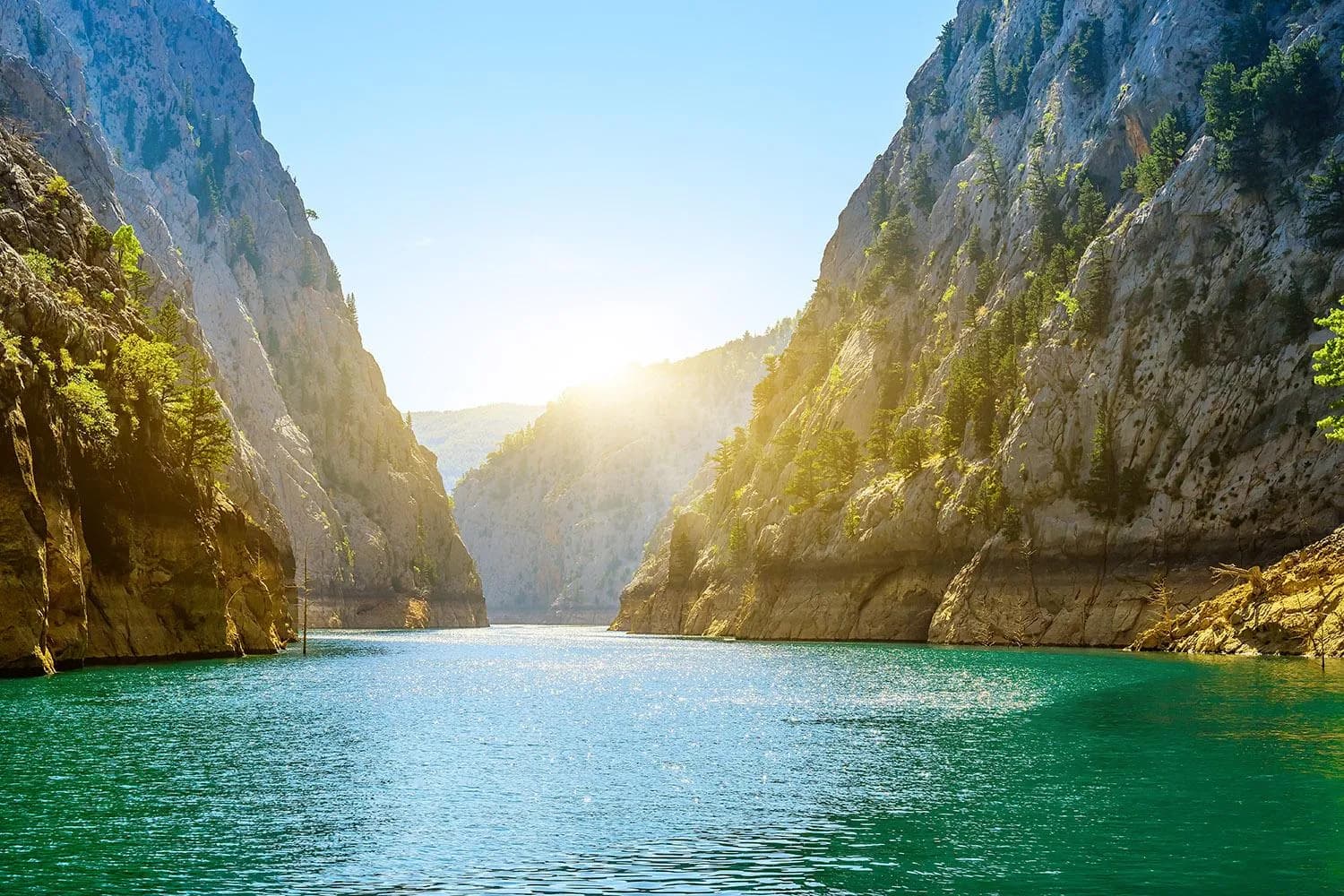 A sightseeing boat cruising on the emerald green water of Green Canyon surrounded by cliffs