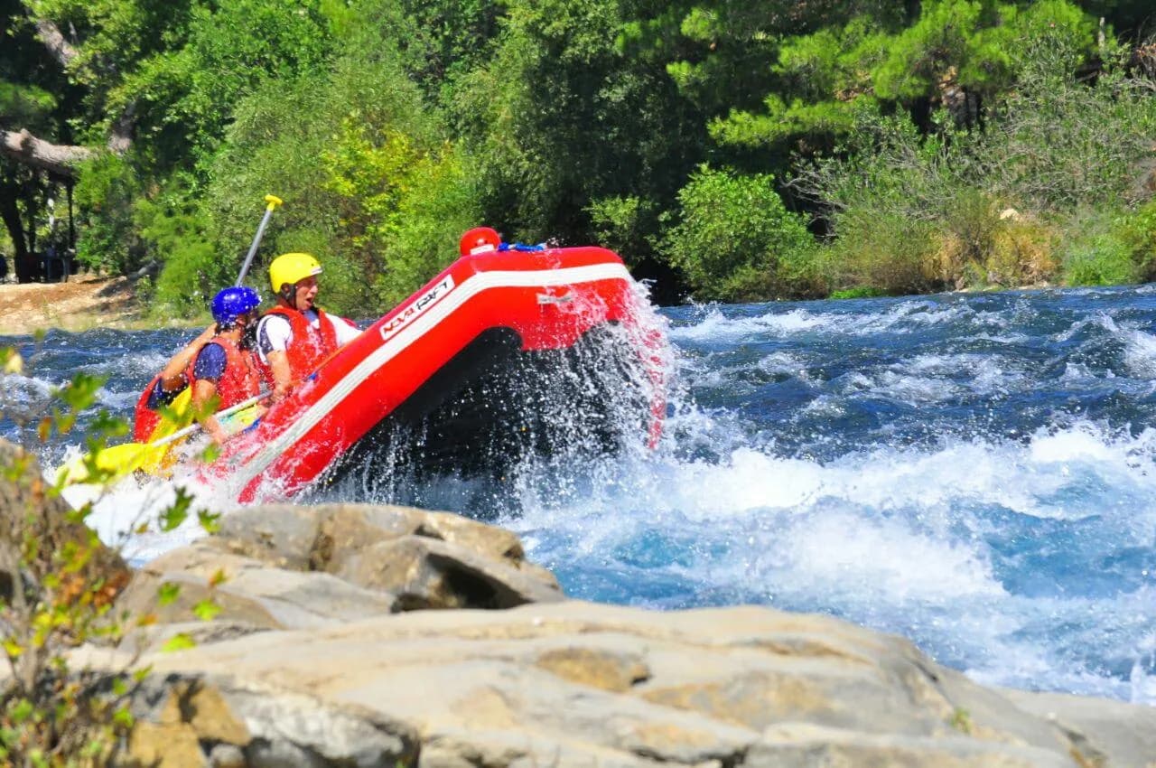 A group of tourists wearing helmets and life jackets paddling a yellow raft on the blue waters of Köprüçay River
